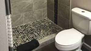 Un baño con ducha, paredes de azulejos, inodoro y una ventana pequeña.
