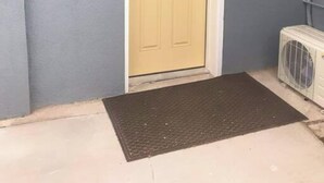 Una puerta amarilla con un ventanal pequeño, un felpudo y una pared gris.