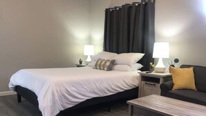 Un dormitorio ordenado con cama, mesitas de noche con lámparas, un sofá y una mesa de centro.