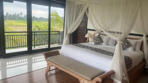 A bedroom with a large bed, a bench, and a balcony with a view of green fields. - Bayad Anyar Ubud Villa (Payangan)