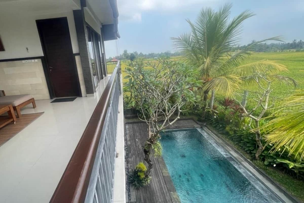 A balcony with a pool, a sofa, and a view of a green landscape.