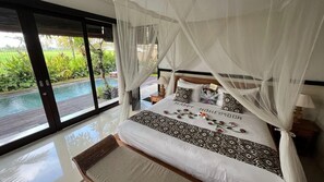 A bedroom with a bed, a bedside table, a nightstand, and a view of a swimming pool. - Bayad Anyar Ubud Villa (Payangan)