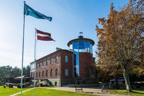 A building with a brick facade, a glass tower, and a flagpole with flags. - Roze Village Jūrnieka Ligzda (Grinvalti)