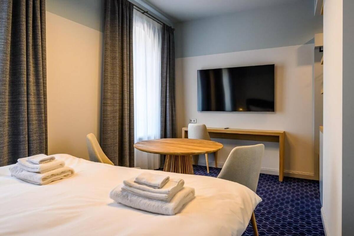 A hotel room with a bed, a desk, a chair, a round table, and a TV mounted on the wall.