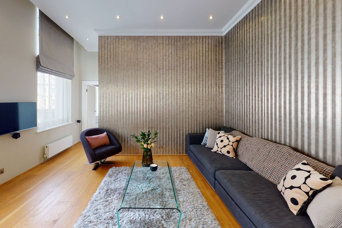 A modern living room with a sofa, a glass coffee table, a TV, and a large window with blinds.
