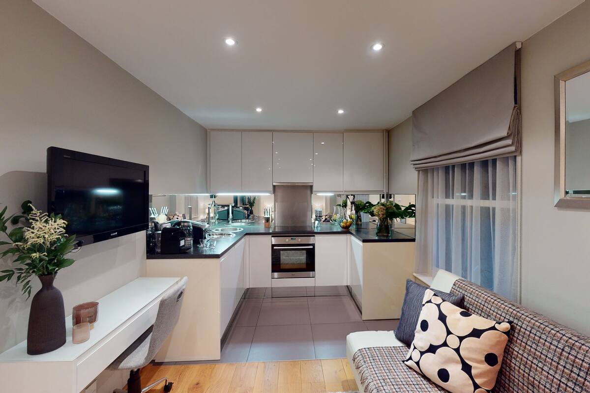 A modern kitchen with a built-in oven, a dining area with a sofa, and a TV mounted on the wall.