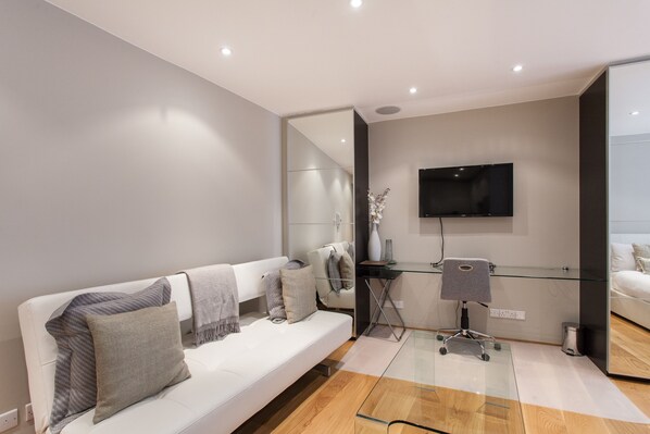 Uma sala de estar moderna com um sofá branco, uma mesa de centro de vidro, uma TV de tela plana na parede e um estilo de decoração minimalista.