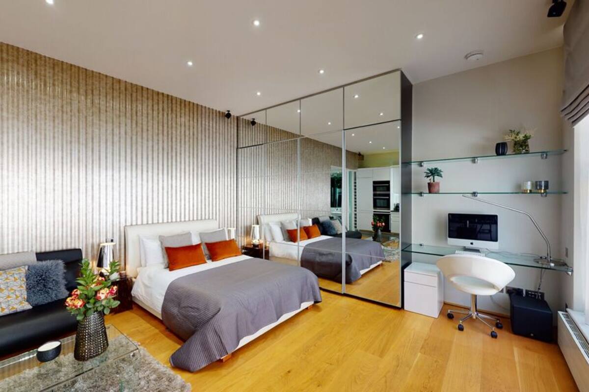 A modern bedroom with a large bed, a sofa, a desk, and a mirror.