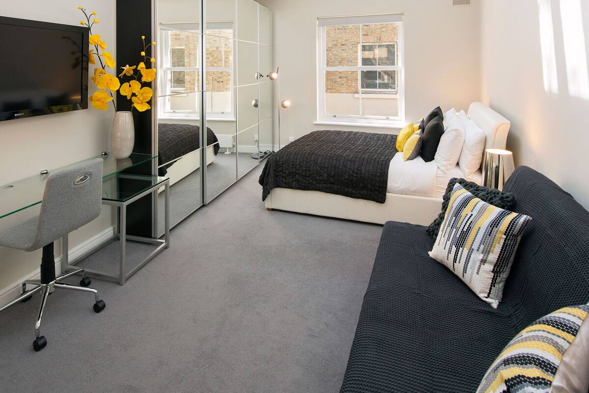 A modern bedroom with a skylight, a bed with pillows, a desk with a chair, and a TV on the wall.