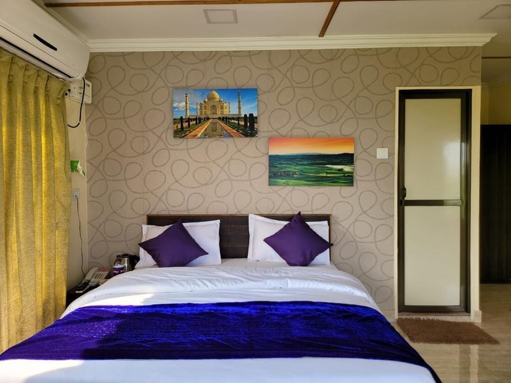 Une chambre d’hôtel avec un lit, une table de chevet, un téléphone et deux tableaux au mur.