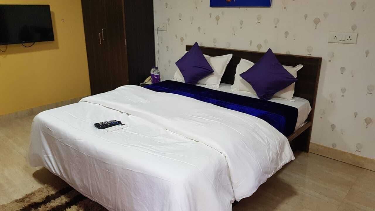 A neatly made bed with a white and blue bedspread, a remote control on the bed, and a wall-mounted TV.