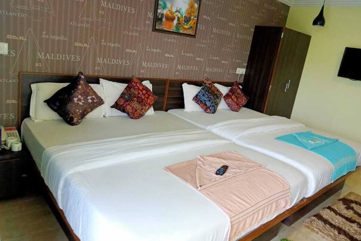 A double bed with white linens, multiple decorative pillows, a framed picture above the bed, and a television mounted on the wall.