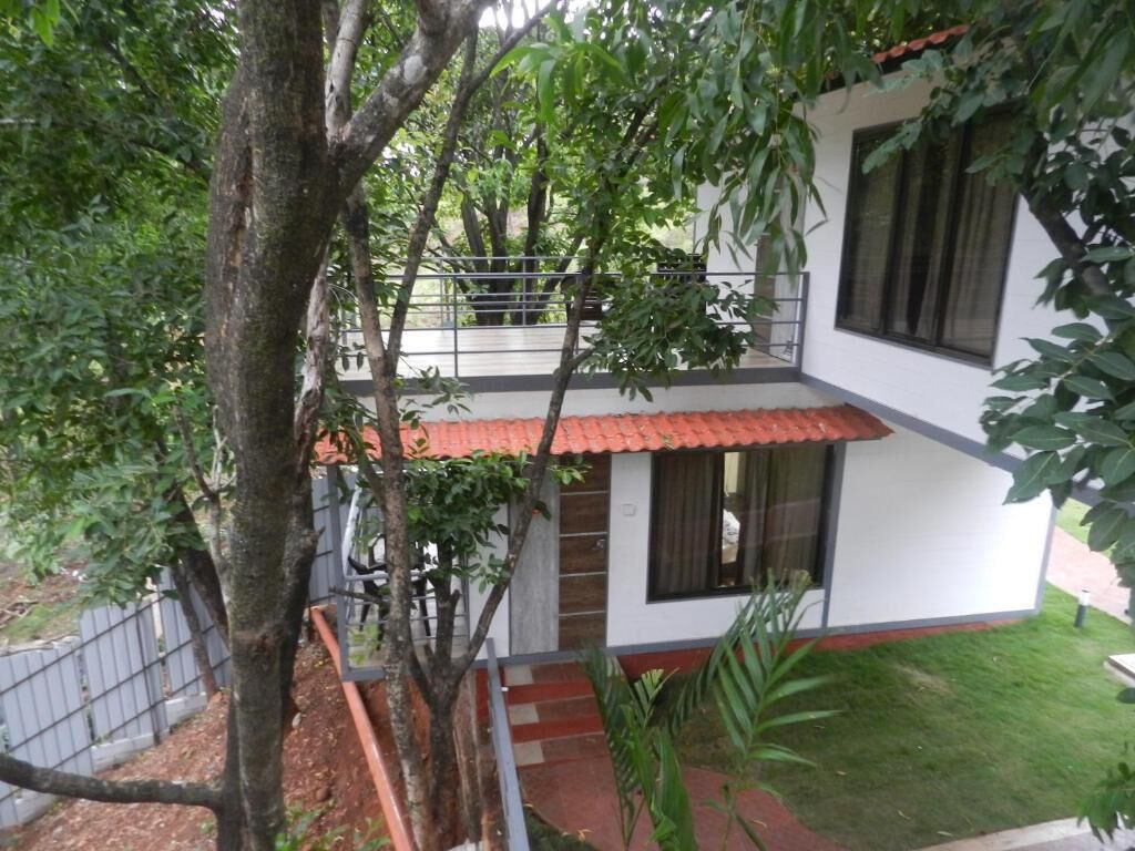 A two-story house with a balcony, surrounded by trees and a small garden.