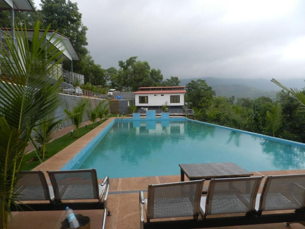 A swimming pool with lounge chairs, a building in the background, and a view of the surrounding landscape.