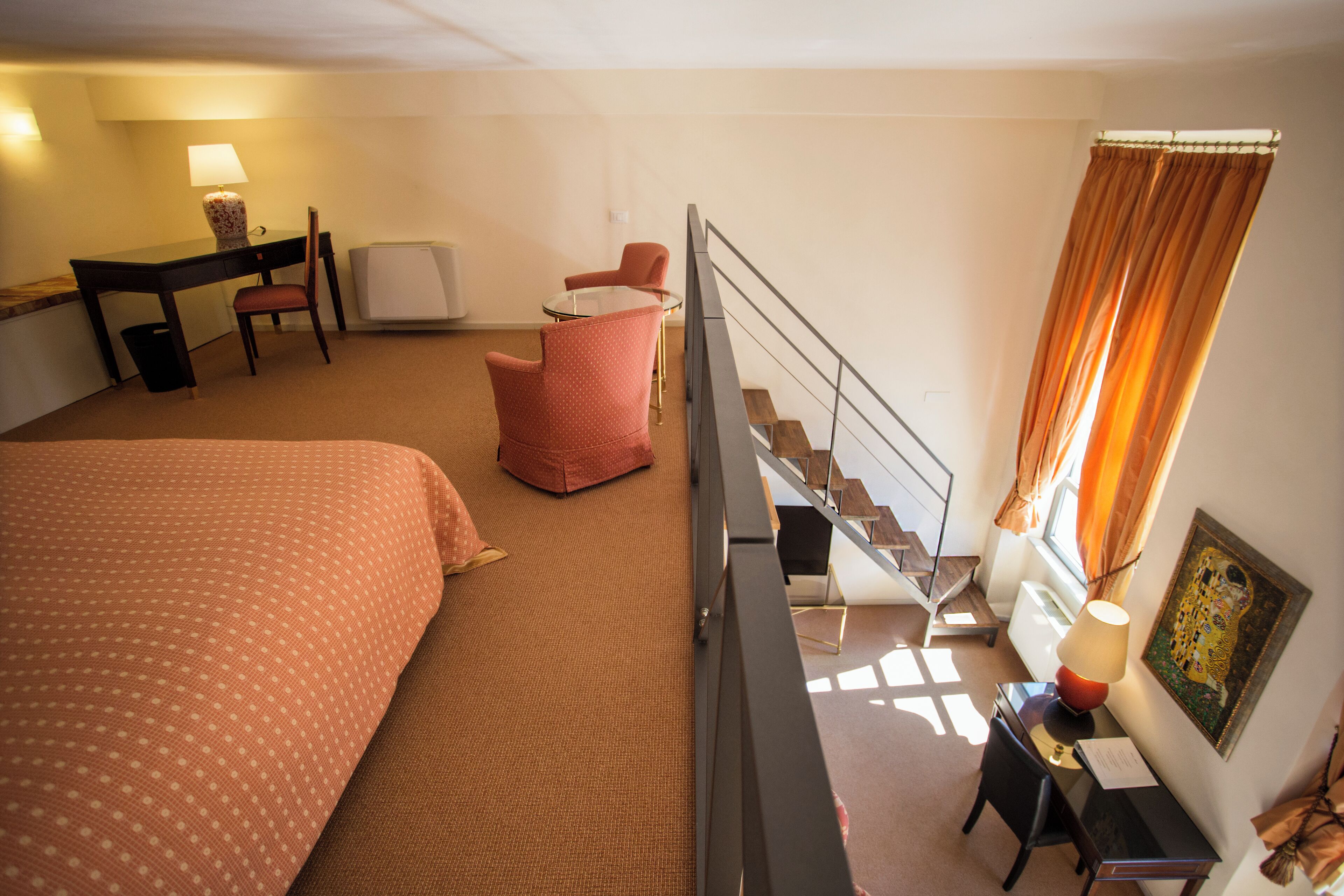 Et hotelværelse med seng, skrivebord, stol, lille bord og en trappe.