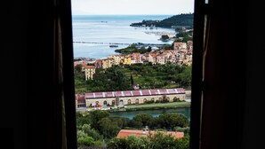 Vista a través de una ventana arqueada de un pueblo costero con edificios, un río y un puente.