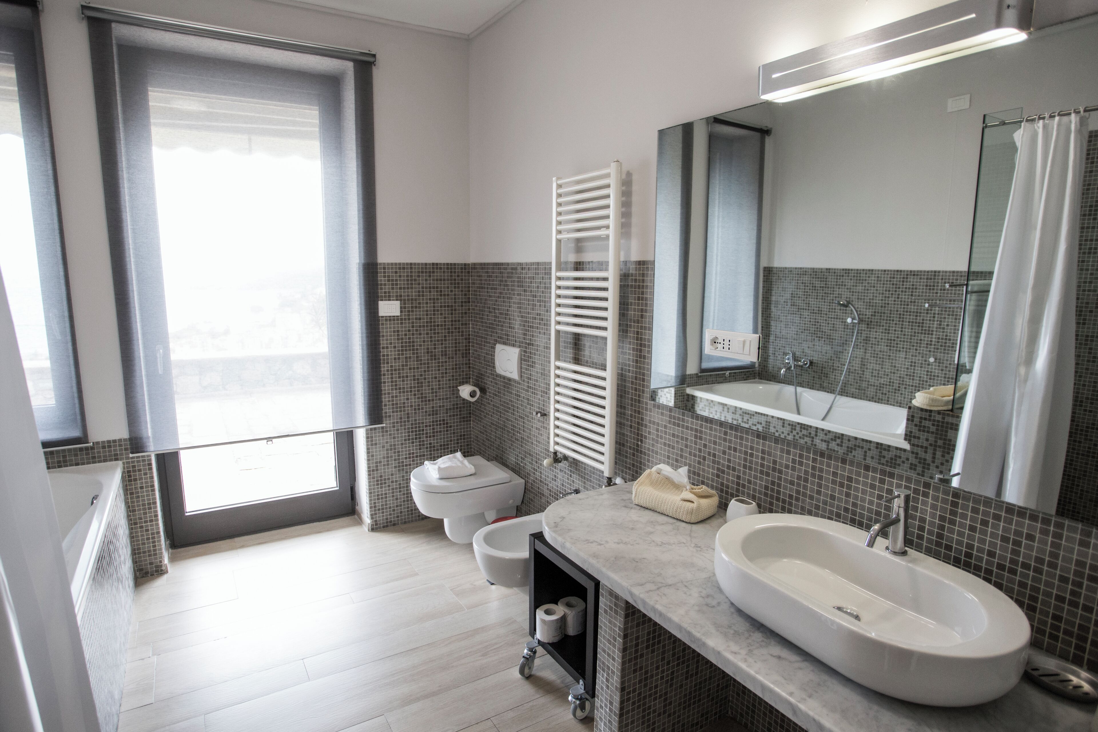 A modern bathroom with a large window, a bathtub, a toilet, and a sink.