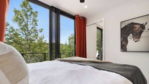 A bedroom with a large window, a bed with white bedding, and a framed picture on the wall. - Luxury Container | Retreat In Bloom • Pool • Sauna (Young Harris)