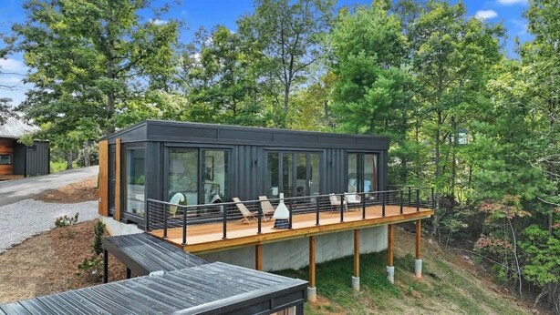 A modern cabin with a deck, large windows, and a view of the surrounding forest. - Luxury Container | Retreat In Bloom • Pool • Sauna (Young Harris)
