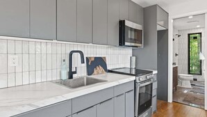 A modern kitchen with grey cabinets, a white countertop, and a built-in oven. - Luxury Container | Retreat In Bloom • Pool • Sauna (Young Harris)