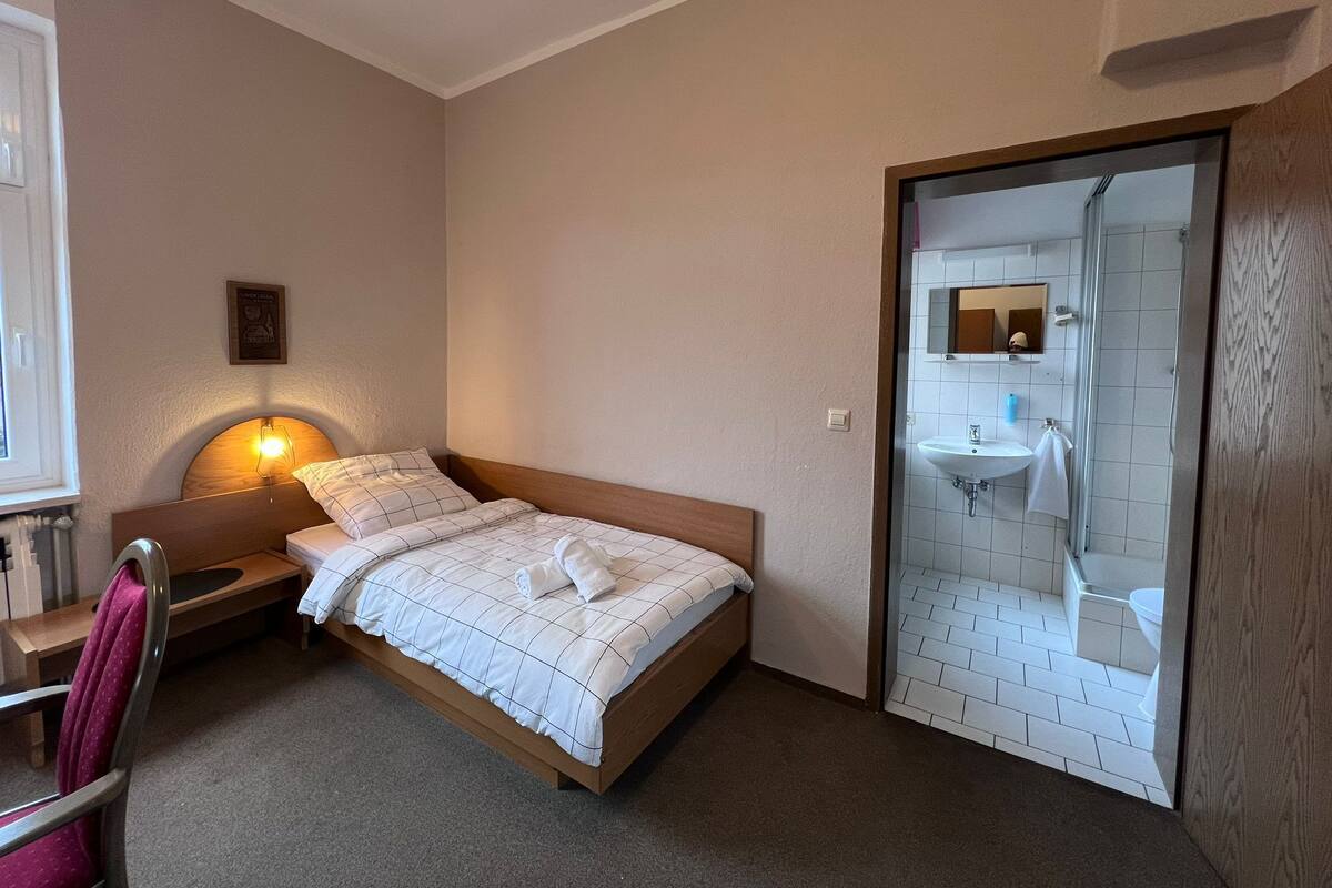 A bedroom with a wooden bed, a nightstand, a lamp, and a view of a bathroom with a shower and sink.