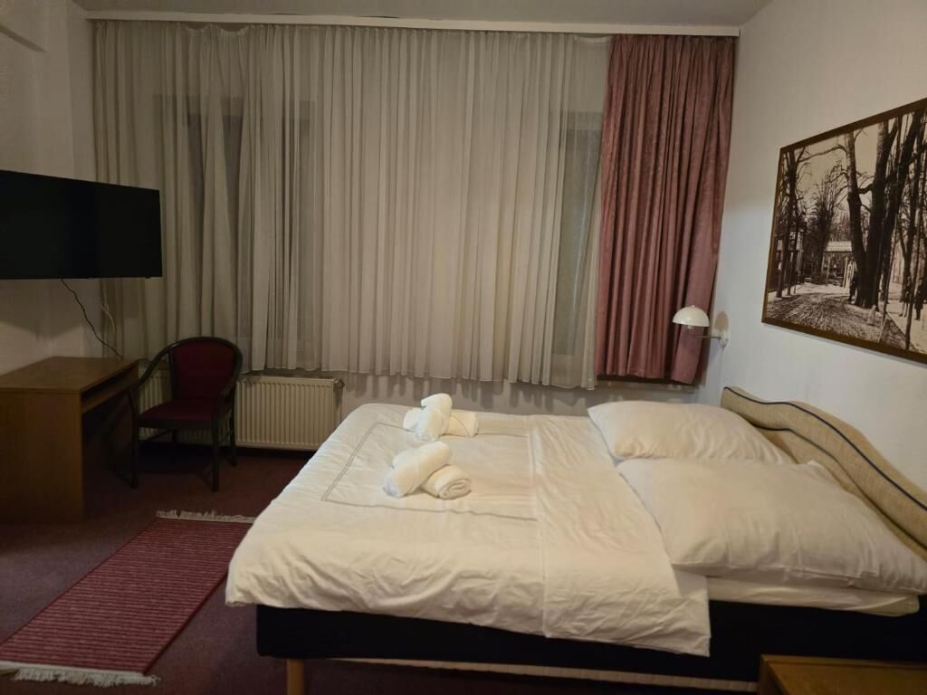 Habitación de hotel con cama, escritorio, silla, televisor y un cuadro en la pared.