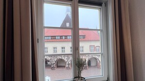 A window with a potted plant, a radiator below, and a view of buildings with red roofs and arches. - Hotel Doko Gardelegen (Gardelegen)