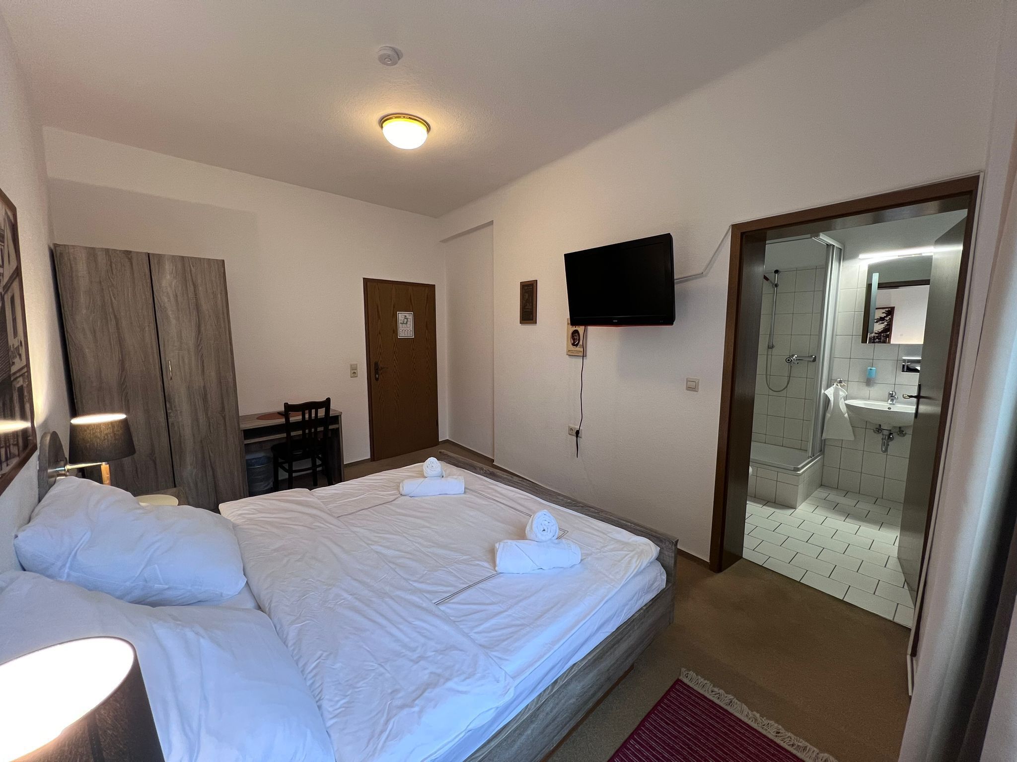 Ein Hotelzimmer mit Bett, Schreibtisch, Stuhl, Fernseher und einem Badezimmer mit Dusche.