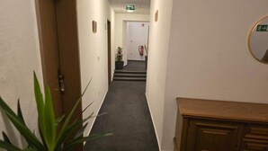 A hallway with carpeted floors, wooden doors, and a wooden bench. - Hotel Doko Gardelegen (Gardelegen)