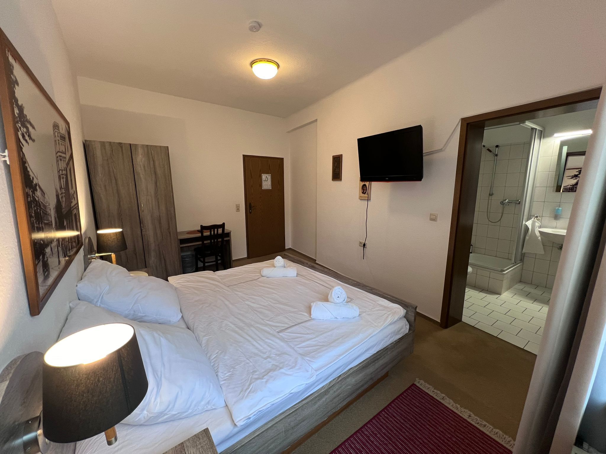 Ein Hotelzimmer mit Bett, Schreibtisch, Stuhl, Fernseher und Duschbereich.