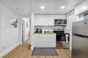 Una cocina moderna con armarios blancos, un refrigerador de acero inoxidable, un microondas y un horno.