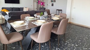 Ein Essbereich mit einem Tisch für vier Personen, umgeben von Stühlen, in einer modernen Wohnung mit einer Couch und einem Flachbildfernseher im Hintergrund.