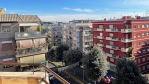 Ein mehrstöckiges Wohngebäude mit Balkonen, blauem Himmel und einer Straße mit parkenden Autos.