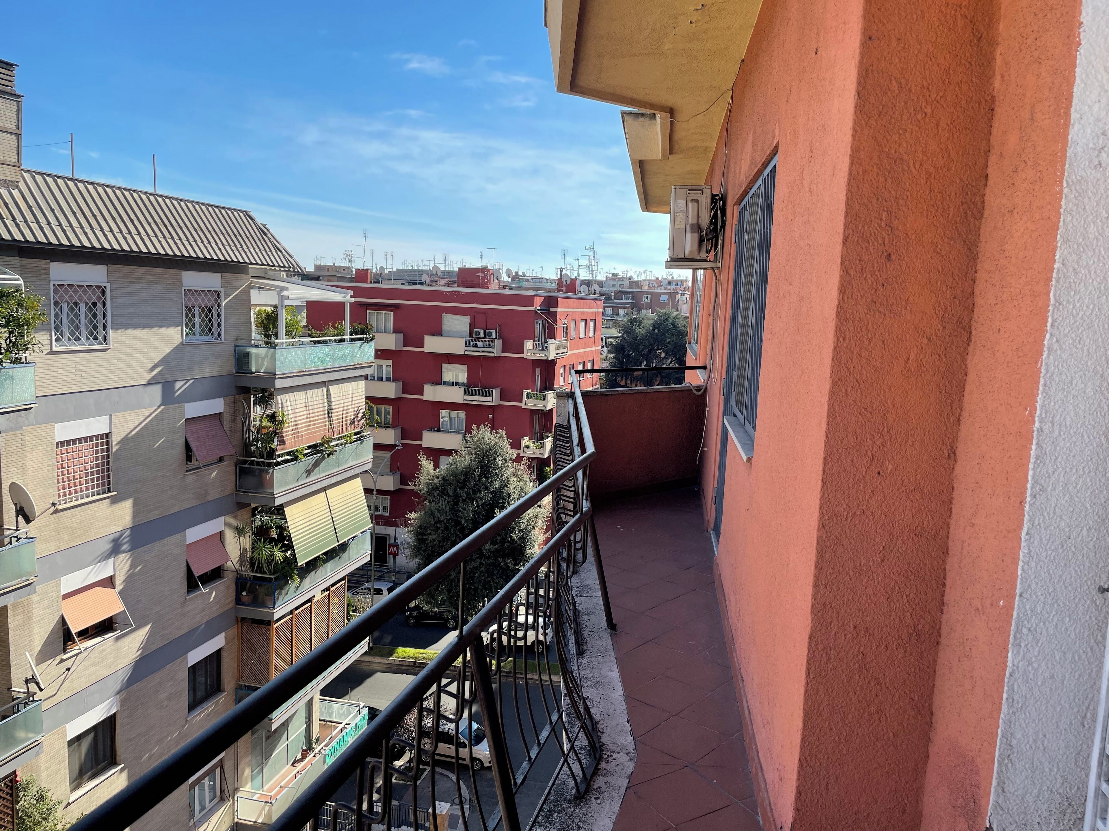 A balcony with a view of neighboring buildings, a metal railing, and a clear sky.