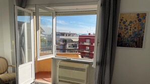 Ein Hotelzimmer mit Bett, einem Fenster mit Blick auf Gebäude, einem Heizkörper und einem Bild an der Wand.