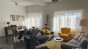 Ein modernes Wohnzimmer mit grauem Sofa, gelbem Sessel und einem Essbereich mit Tisch und Stühlen.