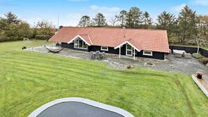A house with a red-tiled roof, a patio with outdoor furniture, and a trampoline in the foreground. - Cozy home in Spøttrup with WiFi (Spøttrup)