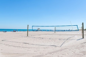 Una cancha de voleibol de playa con una red, rodeada de arena y un cielo azul despejado.