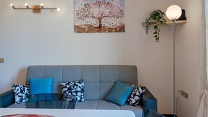 A modern living room with a grey sofa, two patterned cushions, a glass coffee table, a wall-mounted light fixture, a painting of a tree, a floor lamp, and a potted plant. - Adele's House - with pool terrace and WiFi (Sirmione)