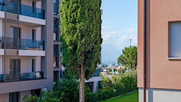 A modern apartment building with balconies, a well-maintained lawn, and a tall tree in the foreground. - Adele's House - with pool terrace and WiFi (Sirmione)