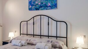 A neatly made bed with a quilt, two rolled towels, and a painting of water lilies on the wall. - Adele's House - with pool terrace and WiFi (Sirmione)