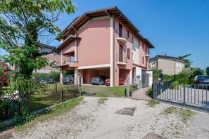 A multi-story residential building with a red facade, a covered parking area, and a gravel driveway. - Adele's House - with pool terrace and WiFi (Sirmione)