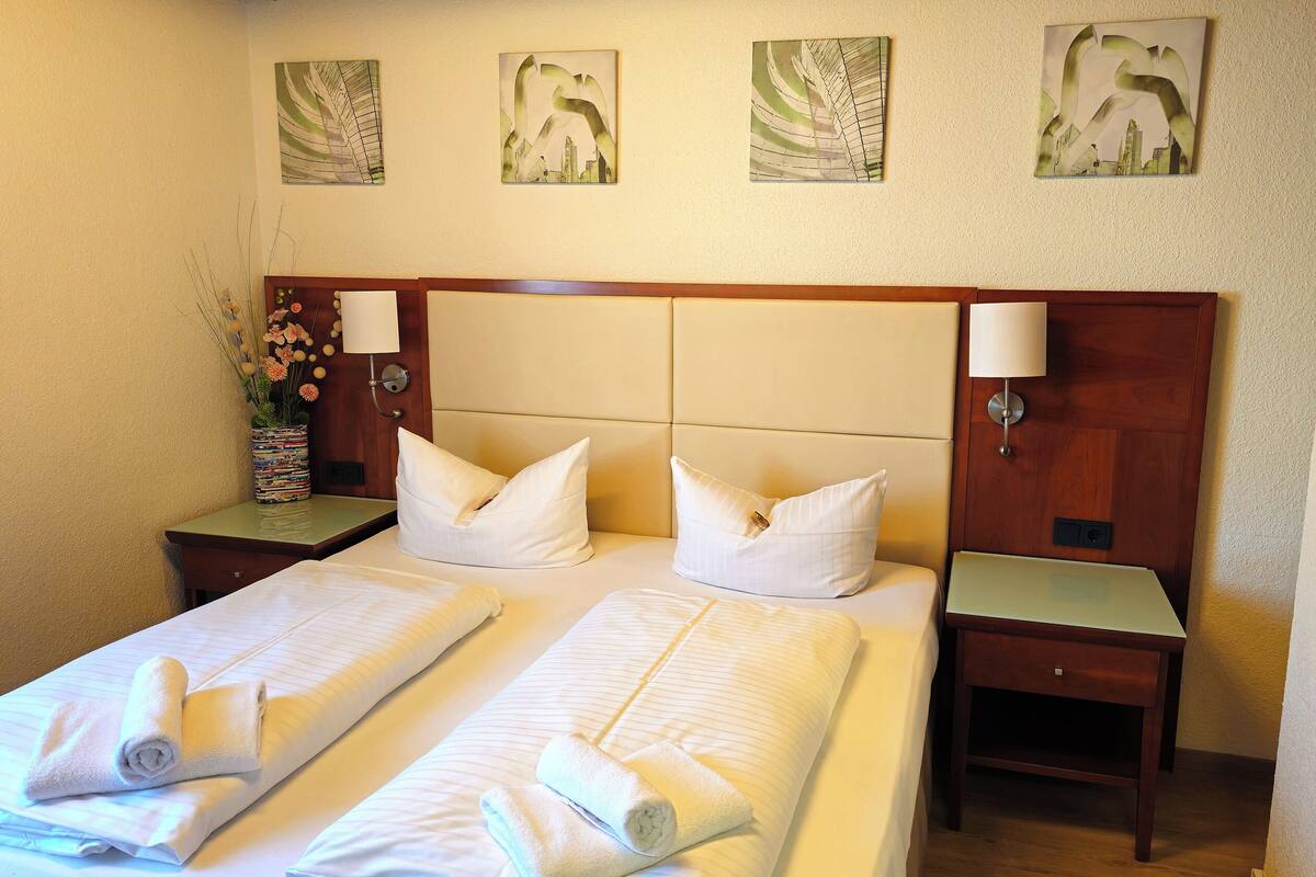 Une chambre d’hôtel avec deux lits, chacun doté de draps et d’oreillers blancs, d’une tête de lit en bois et d’une table de chevet avec une lampe.