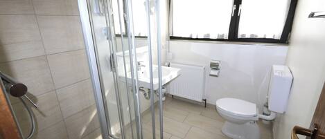 A bathroom with a shower, sink, toilet, and window.