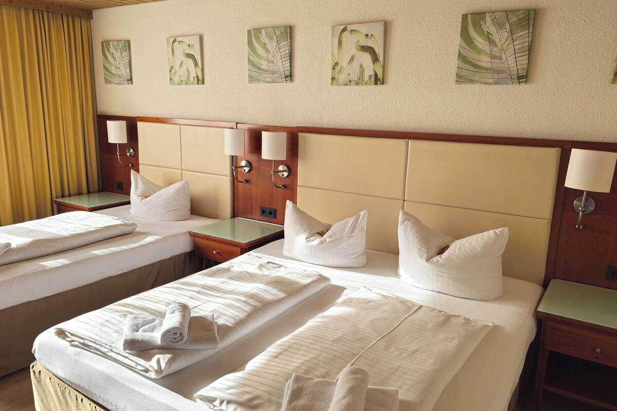 Une chambre d’hôtel avec deux lits, chacun équipé d’un oreiller et d’une serviette roulée. Des lampes murales et des œuvres d’art sont disposées au-dessus des lits.