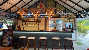 A bar with a high ceiling, hanging light fixtures, and a counter with stools. - White Beach Hostel (Koh Rong)