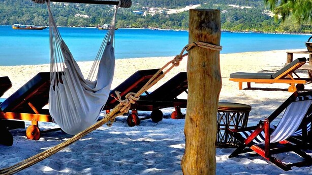 A hammock tied to a wooden post on a sandy beach with lounge chairs and a view of the sea. - White Beach Hostel (Koh Rong)