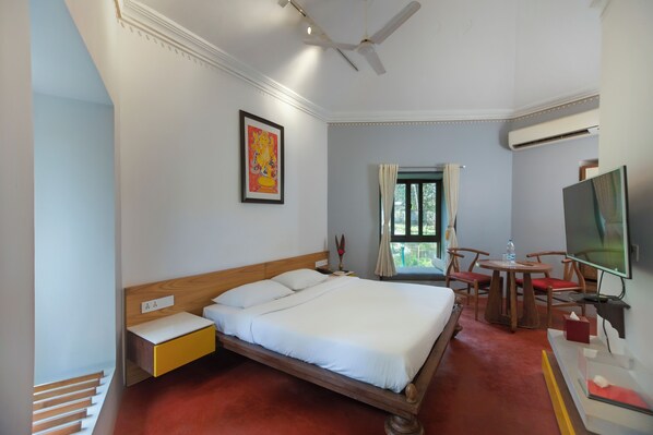 Una habitación de hotel con cama, escritorio, silla, televisor y ventana con cortinas.