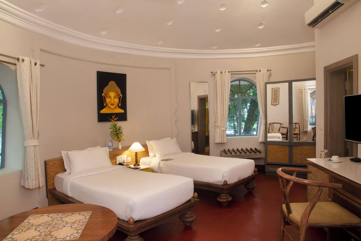 A hotel room with two beds, a wooden chair, a table, and a TV.