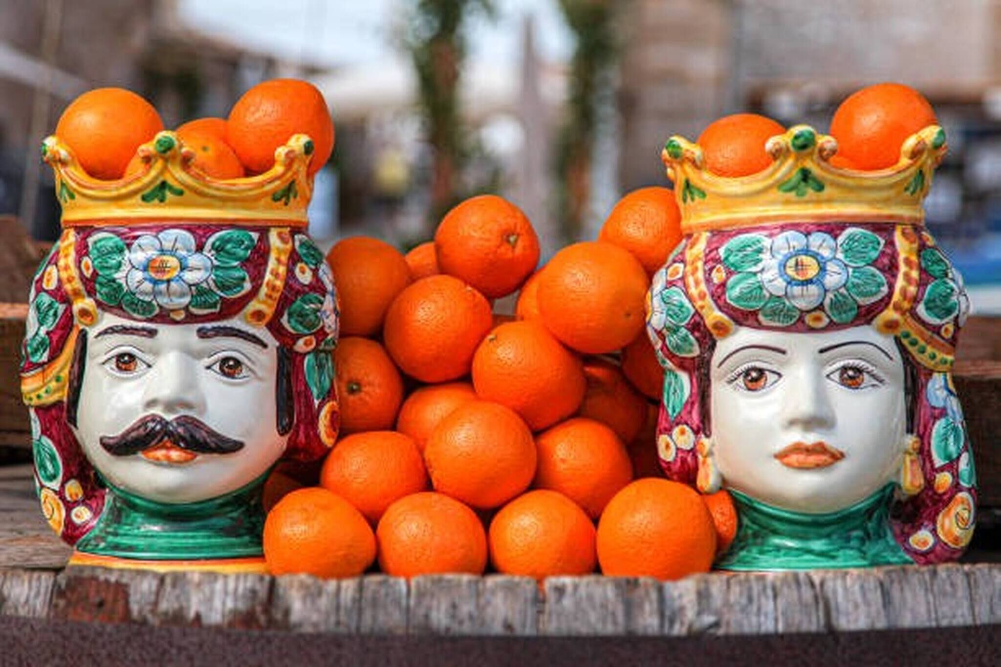 Two ornate ceramic vases with orange fruits on top, placed on a wooden surface.